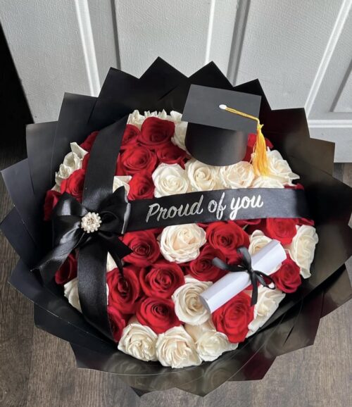 Bouquet of red and white roses wrapped in black paper with a small graduation cap ornament and a 'Proud of you' ribbon.