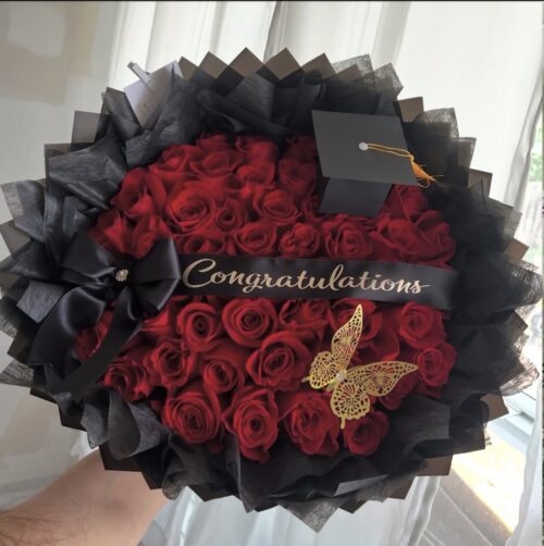 Bouquet of red roses with black wrapping and a gold "Congratulations" ribbon, plus a small graduation cap decoration and butterfly embellishment.