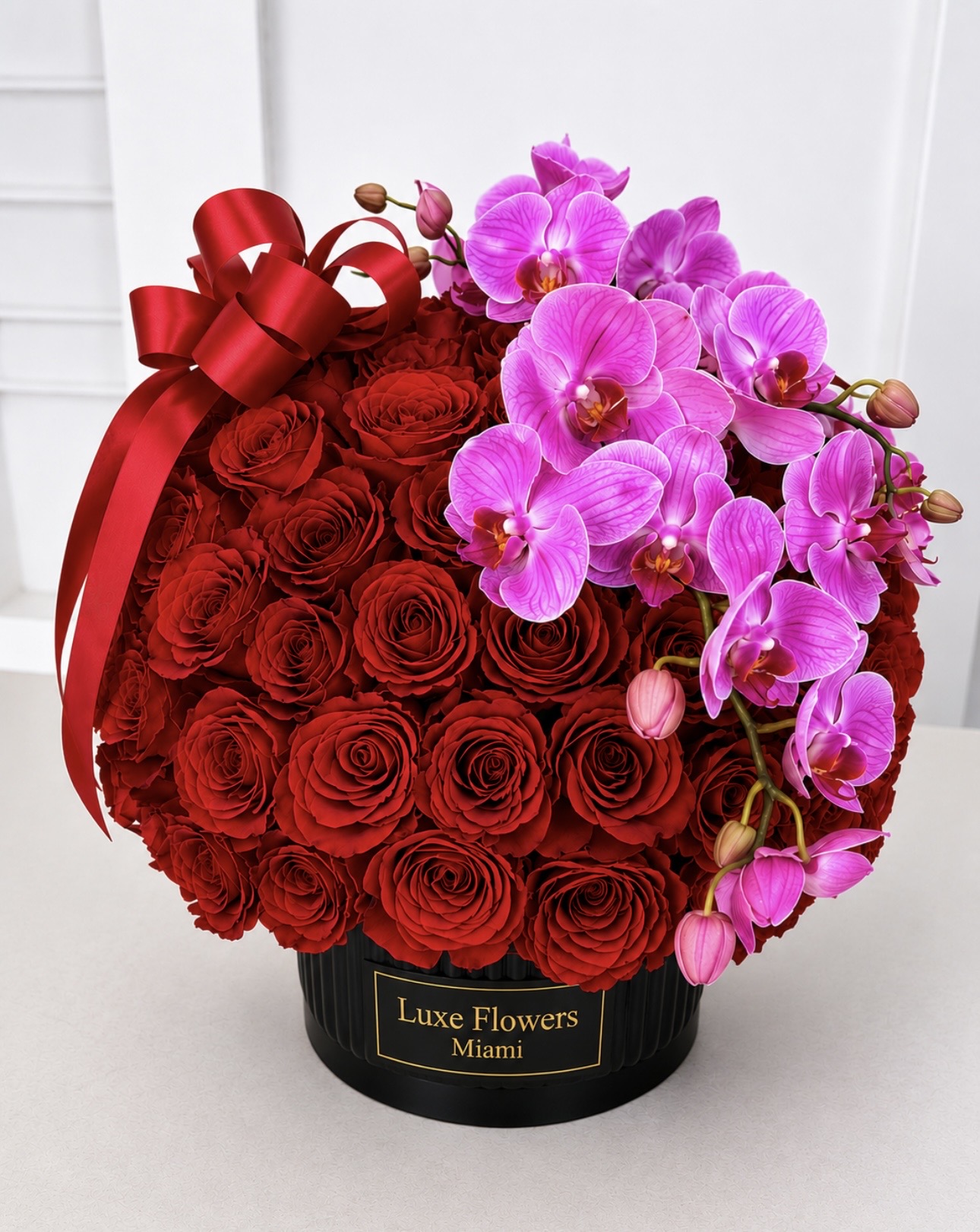 Bouquet of red roses and pink orchids in a black Luxe Flowers Miami hatbox with a red ribbon.
